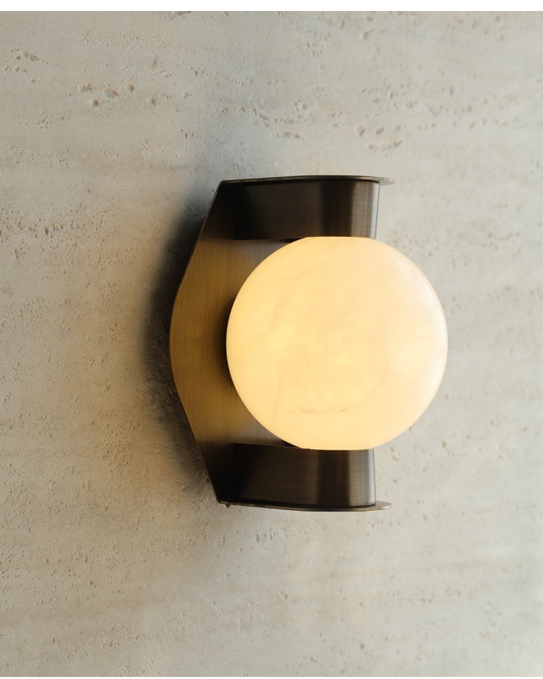 The Clérachic Orb sconce lit against travertine, glow catching the stone's open grain.