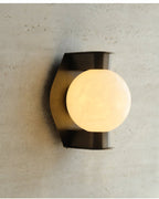The Clérachic Orb sconce lit against travertine, glow catching the stone's open grain.