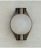 Clérachic Orb sconce unlit on travertine, frosted globe reading cool white against the metal.