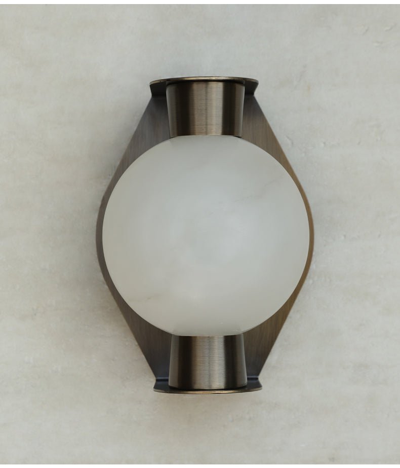 Clérachic Orb sconce unlit on travertine, frosted globe reading cool white against the metal.