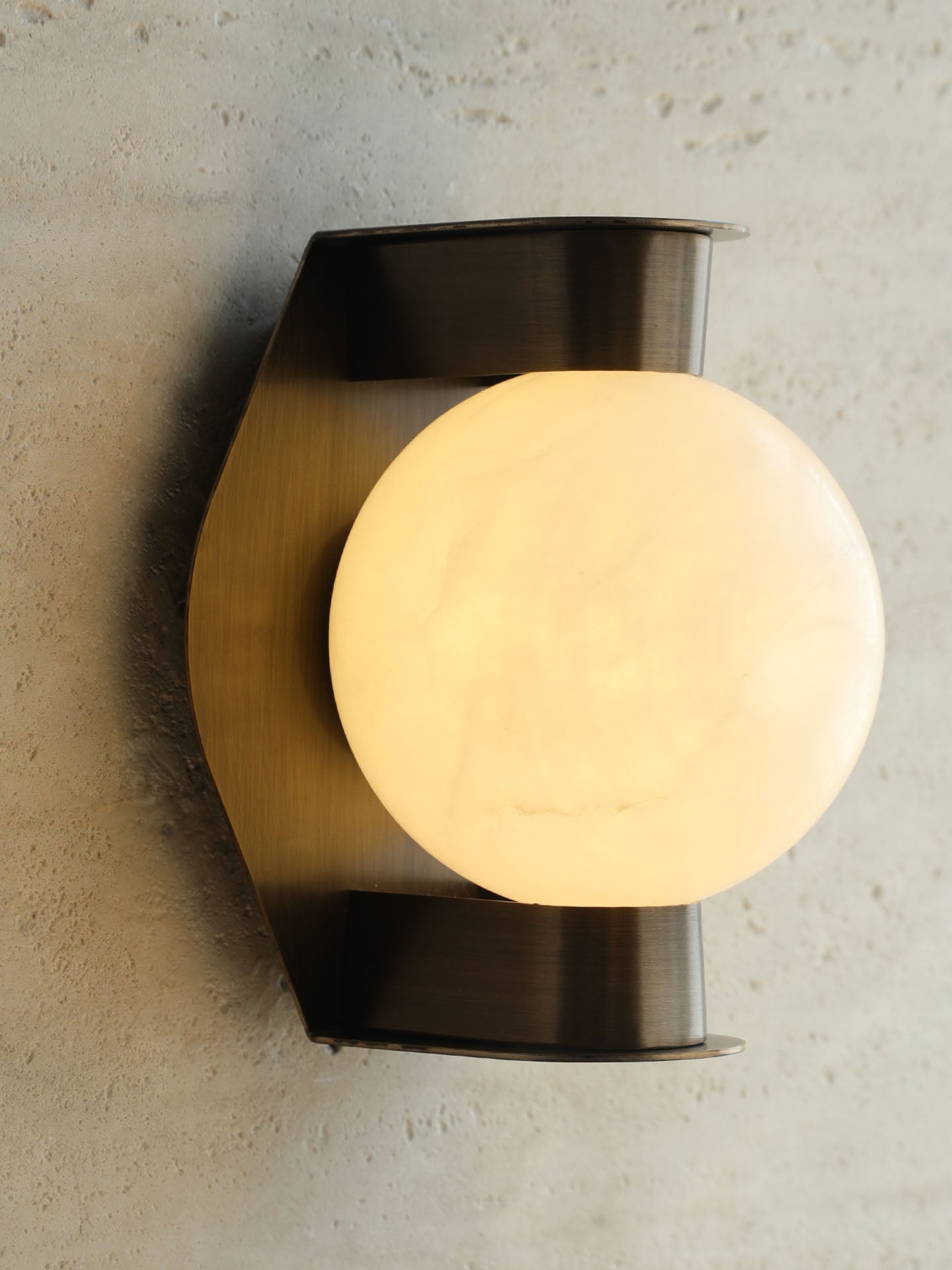 The Clérachic Orb sconce angled on rough plaster, warm light raking across the wall.