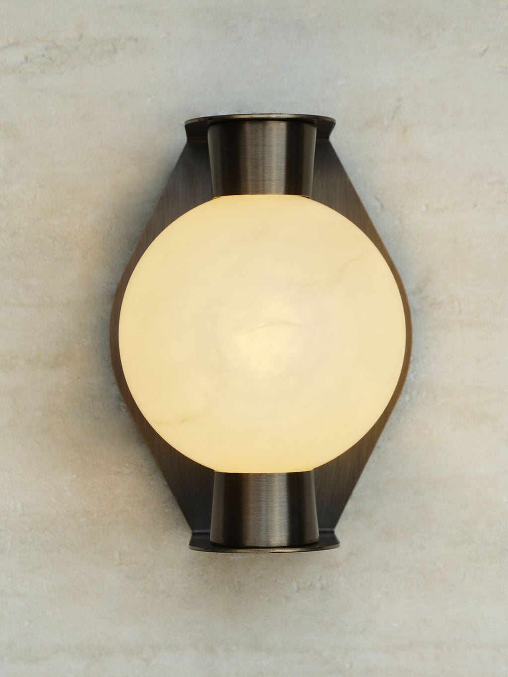 Clérachic Orb sconce lit on a travertine wall, an even amber glow through the stone sphere.