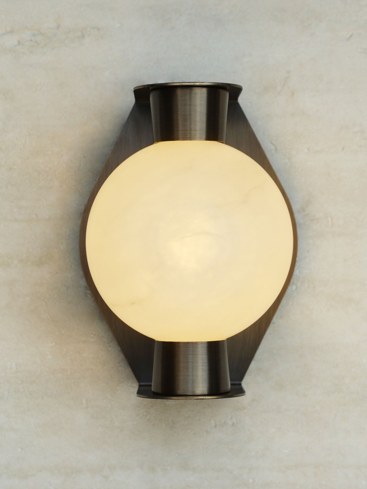 Clérachic Orb sconce lit on a travertine wall, an even amber glow through the stone sphere.