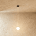 Clérachic single-ball orb pendant light in a matte black finish, glowing warm against a lime-plaster wall backdrop.