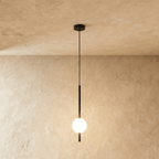 Clérachic single-ball orb pendant light in a matte black finish, glowing warm against a lime-plaster wall backdrop.