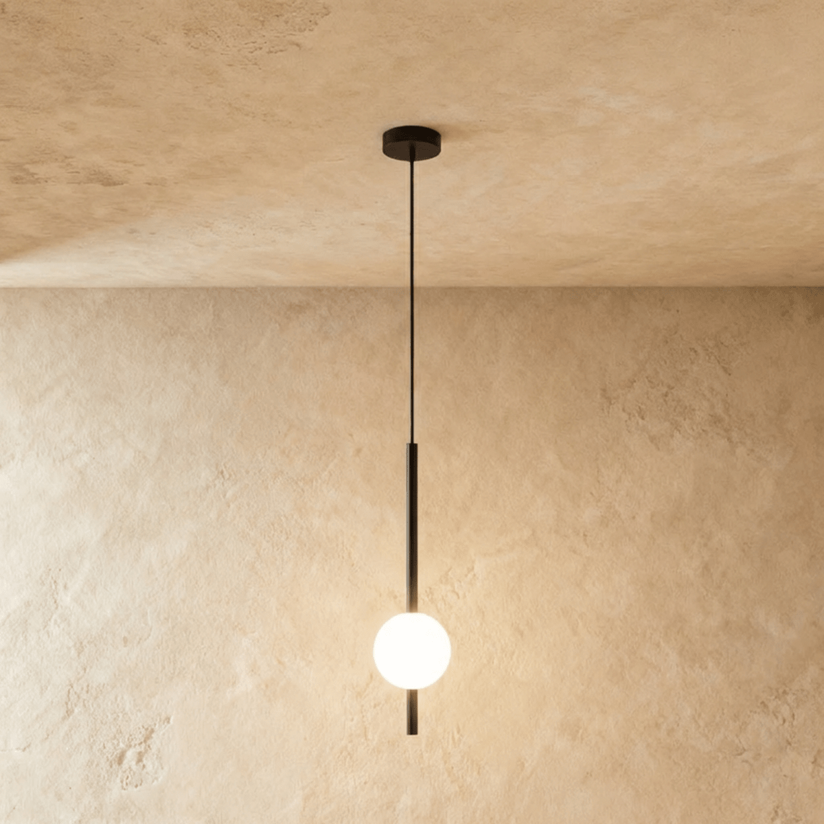 Clérachic single-ball orb pendant light in a matte black finish, glowing warm against a lime-plaster wall backdrop.
