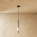Clérachic single-ball orb pendant light in a matte black finish, unlit against a lime-plaster wall backdrop.