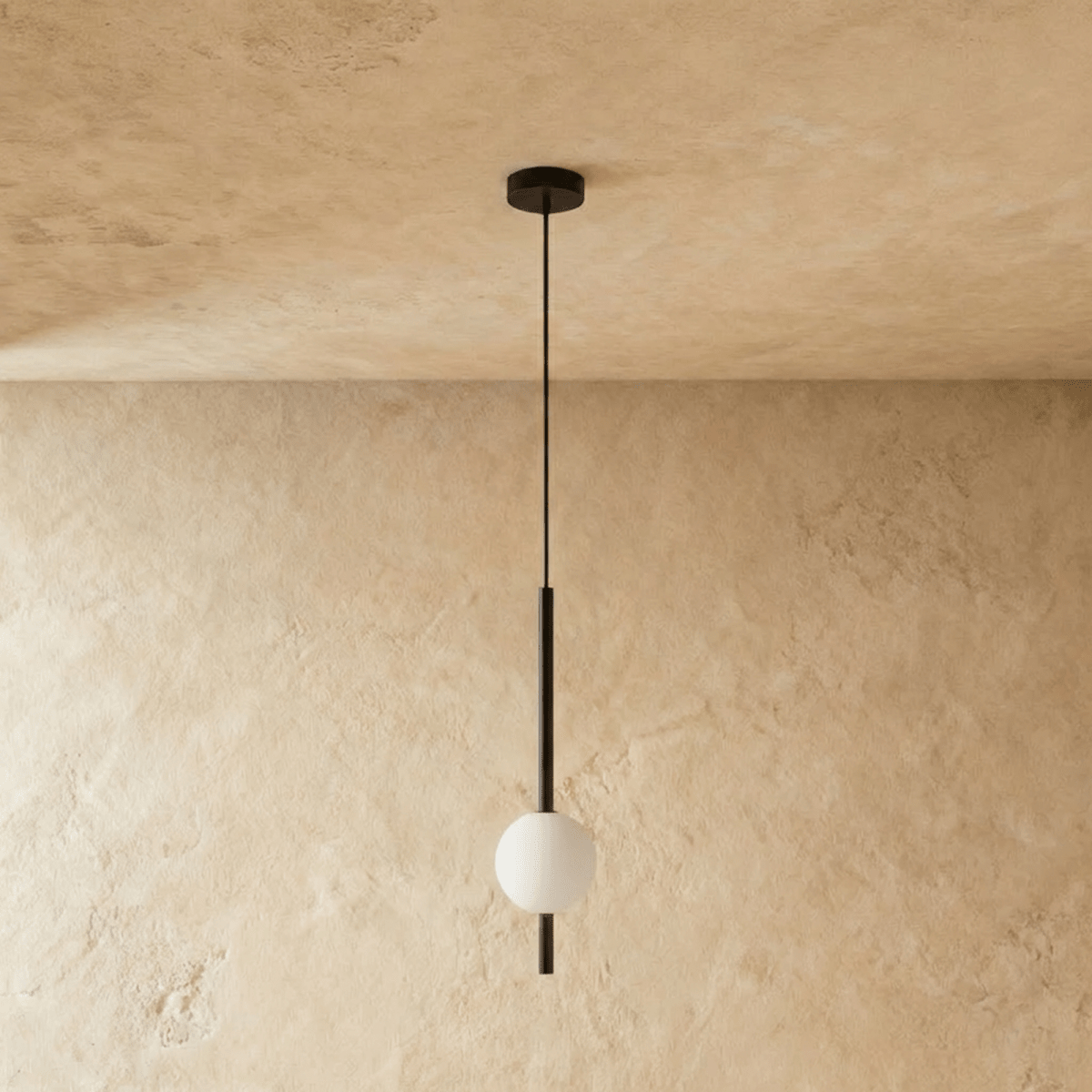 Clérachic single-ball orb pendant light in a matte black finish, unlit against a lime-plaster wall backdrop.