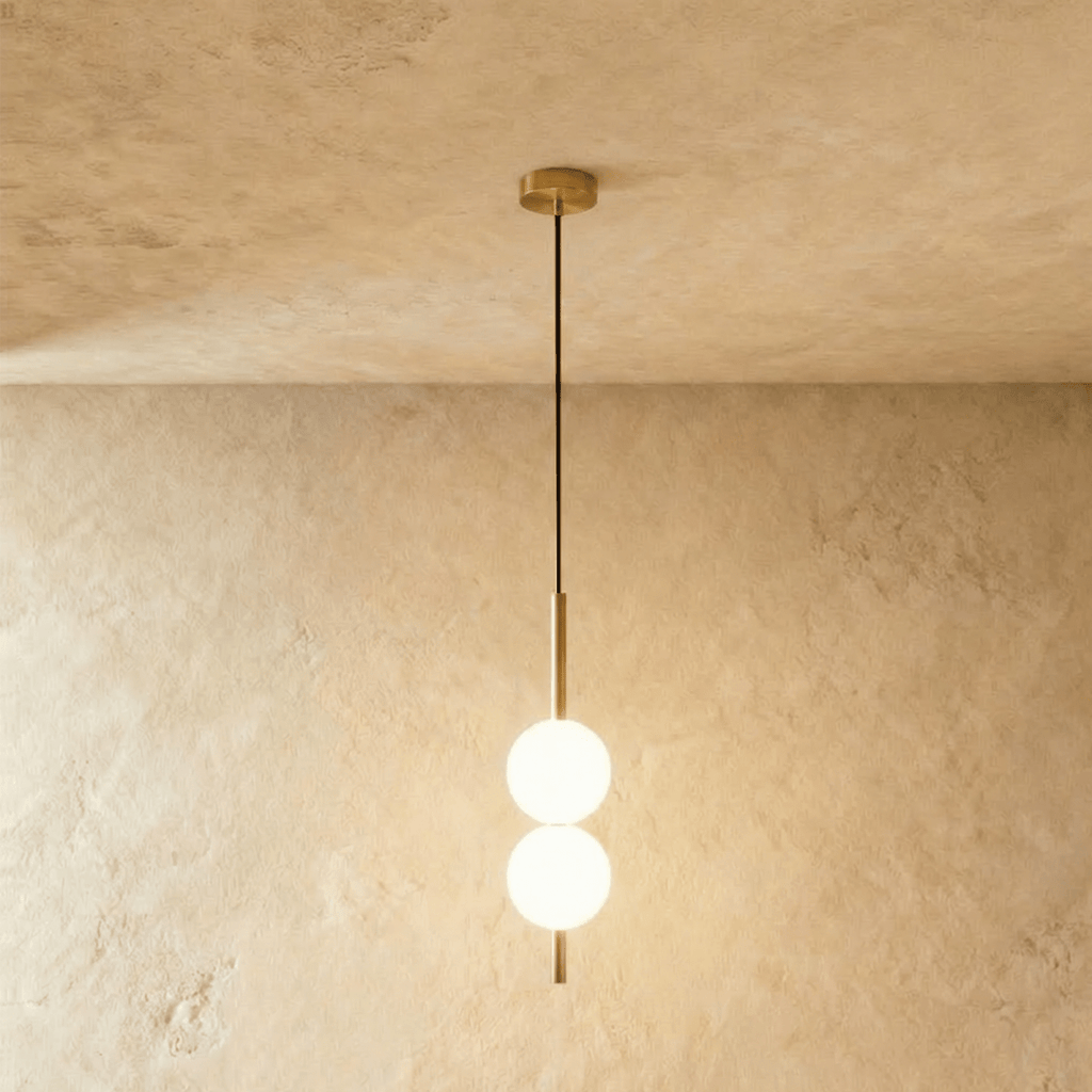 Clérachic two-ball orb pendant light in a brushed brass finish, both globes glowing warm on one slim rod.