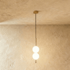 Clérachic two-ball orb pendant light in a brushed brass finish, both globes glowing warm on one slim rod.