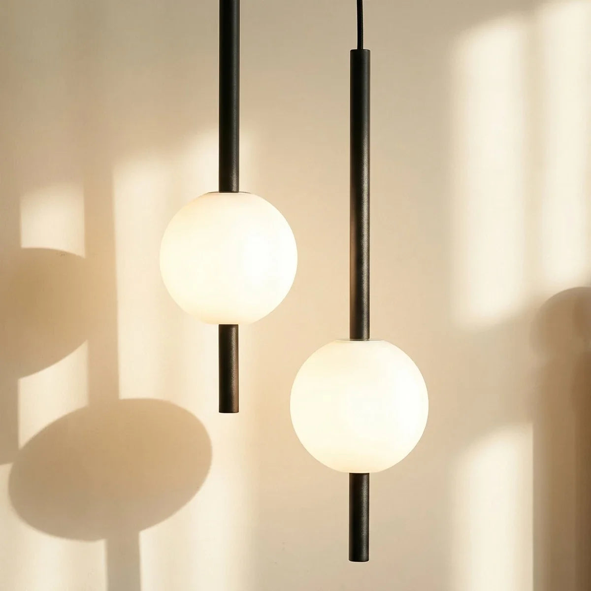 Clérachic twin-head orb pendant light in matte black, close crop of both glass globes glowing against a sunlit wall.
