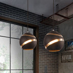 Two black Clérachic glass globe pendant lights glowing above a brick-walled industrial dining nook.