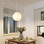 A white Clérachic glass globe pendant light glowing softly over a wood dining table set with green dishware.