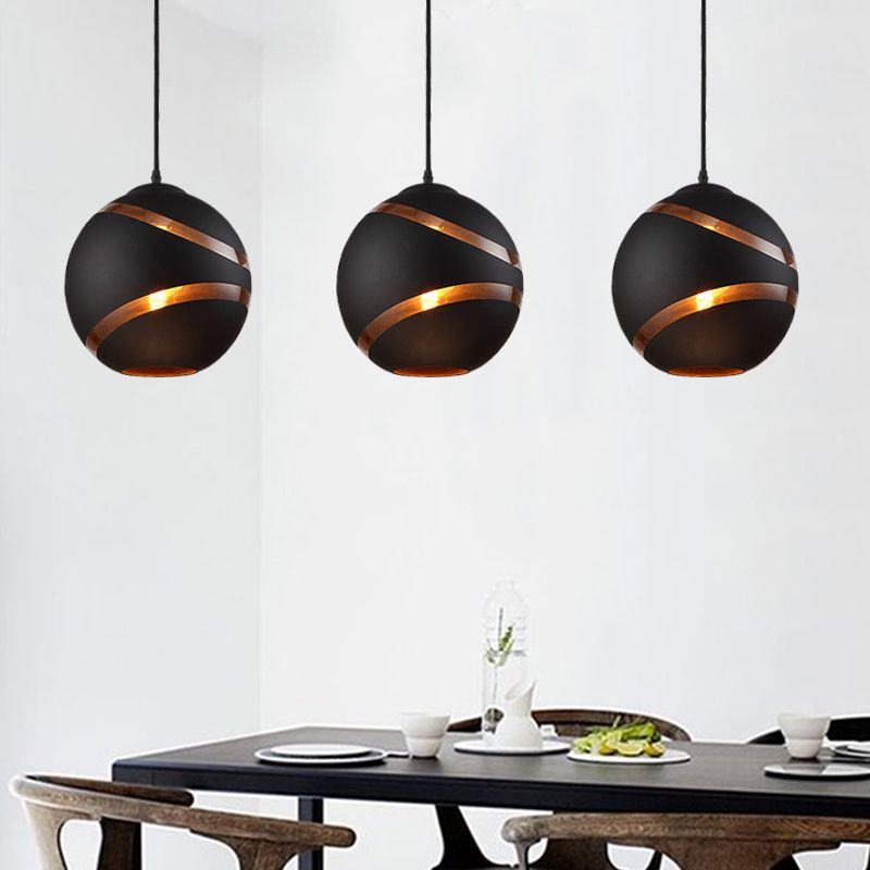 Three black Clérachic glass globe pendant lights spaced above a dark wood dining table, each glowing warmly.