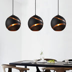 Three black Clérachic glass globe pendant lights spaced above a dark wood dining table, each glowing warmly.