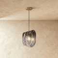 Clérachic single pendant with a smoke-grey gradient glass shade, lit warm from a filament bulb against limewash.