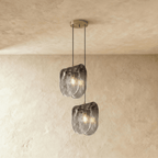 Clérachic two-head glass pendant glowing warm, its rippled smoke-grey shades hanging at two heights on plaster.