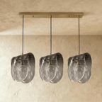 Clérachic three-head linear pendant with smoke-grey glass shades hung from a long brushed gold-tone canopy bar.