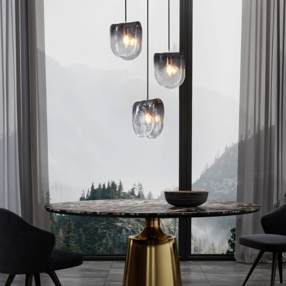 Three Clérachic smoke-grey glass pendants at staggered heights over a round dining table, with a misty forest view.