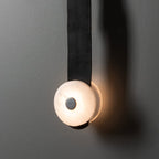 Clérachic Orinos alabaster head lit against a grey wall, warm light spilling around the stone on its black leather strap.