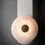 The Clérachic Orinos head in white leather: pale veined alabaster around a brass centre, lit against a dark wall.