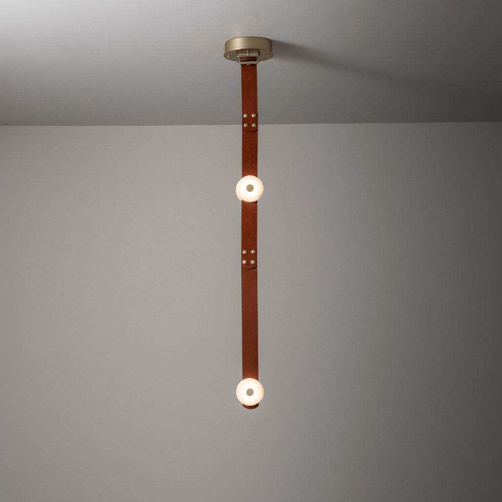 The two-head Clérachic Orinos straight drop, alabaster discs spaced along a riveted cognac strap against a plain wall.