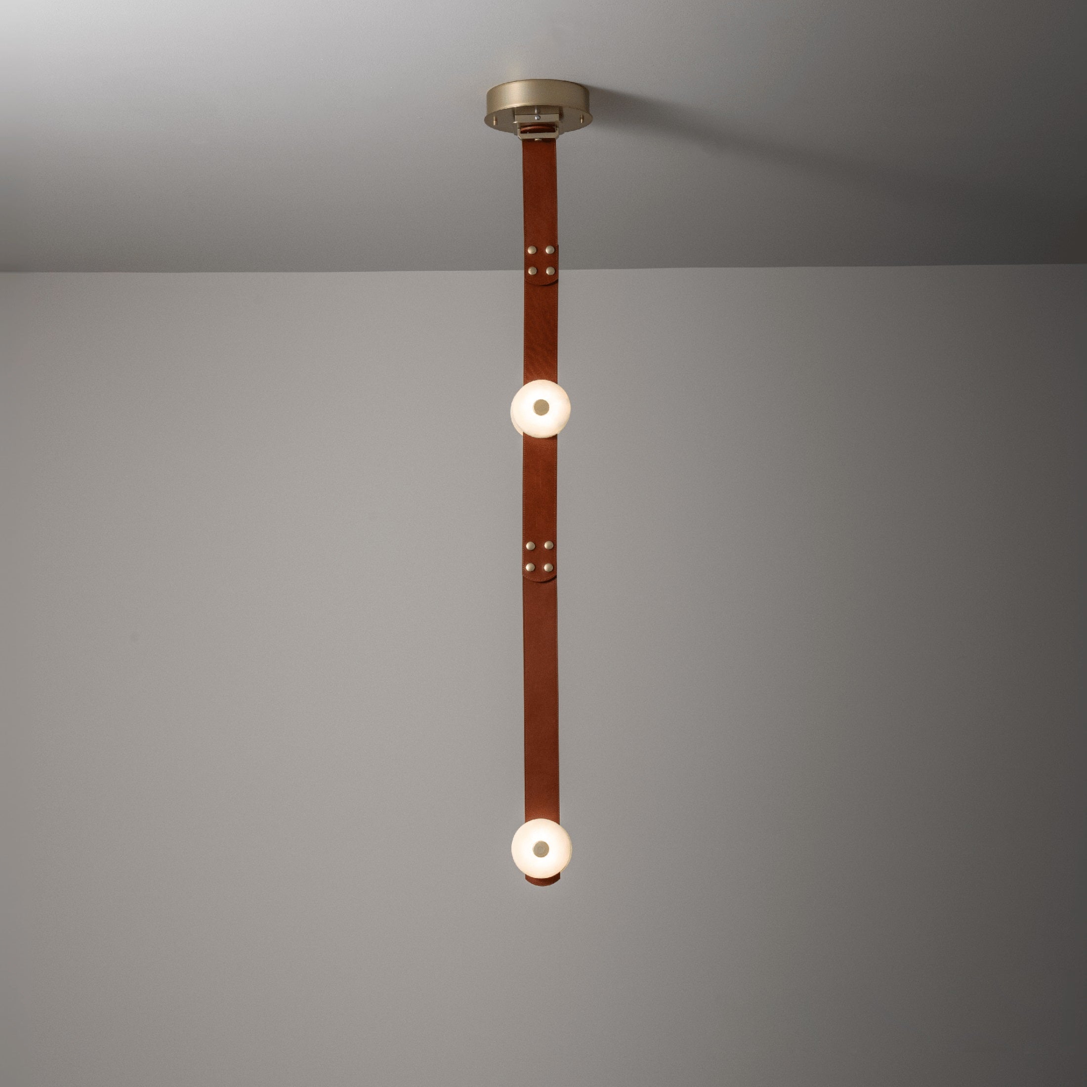 The two-head Clérachic Orinos straight drop, alabaster discs spaced along a riveted cognac strap against a plain wall.