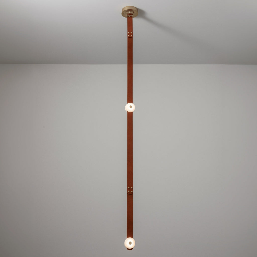 The long-drop Clérachic Orinos run, a riveted cognac strap carrying two lit alabaster heads in a double-height room.