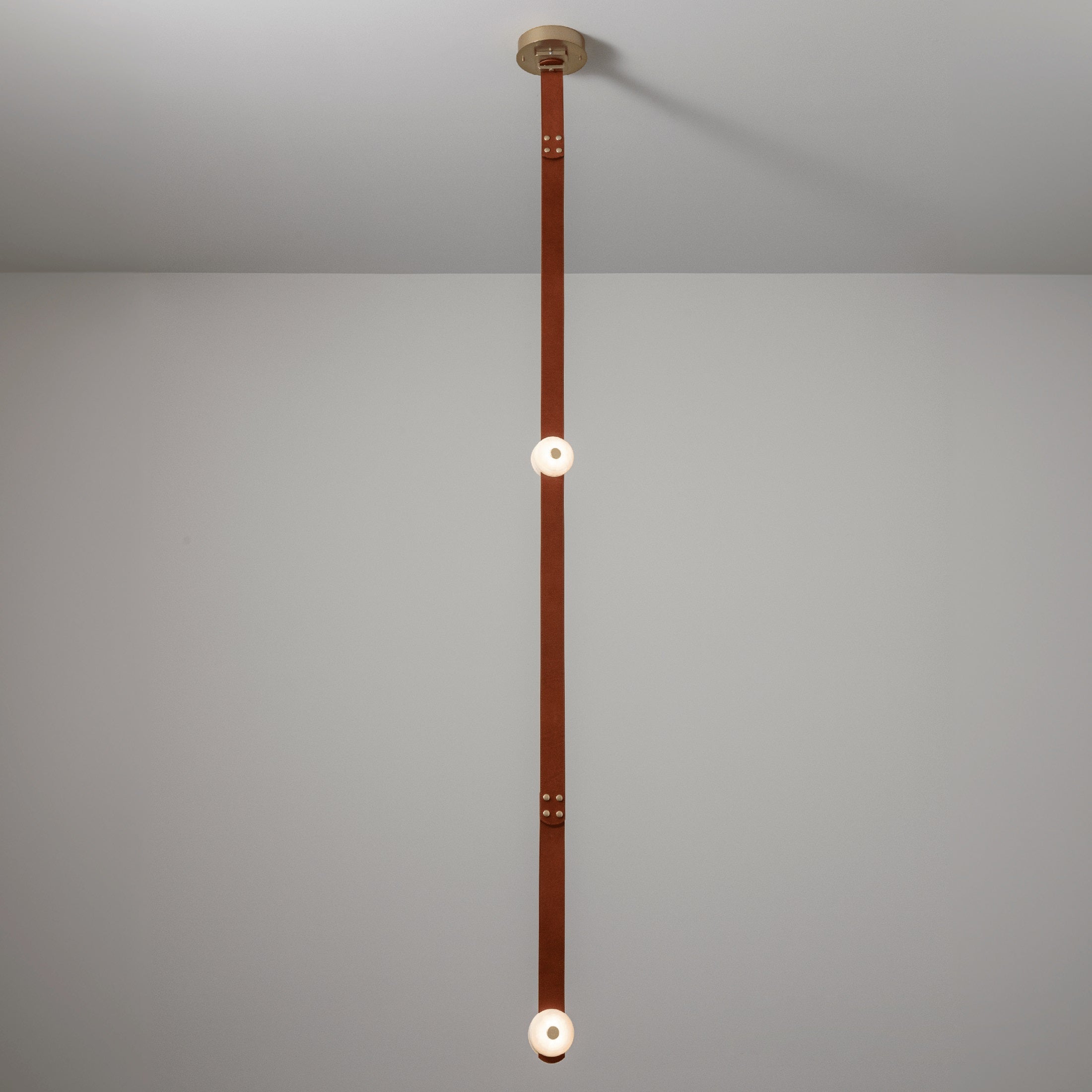 The long-drop Clérachic Orinos run, a riveted cognac strap carrying two lit alabaster heads in a double-height room.