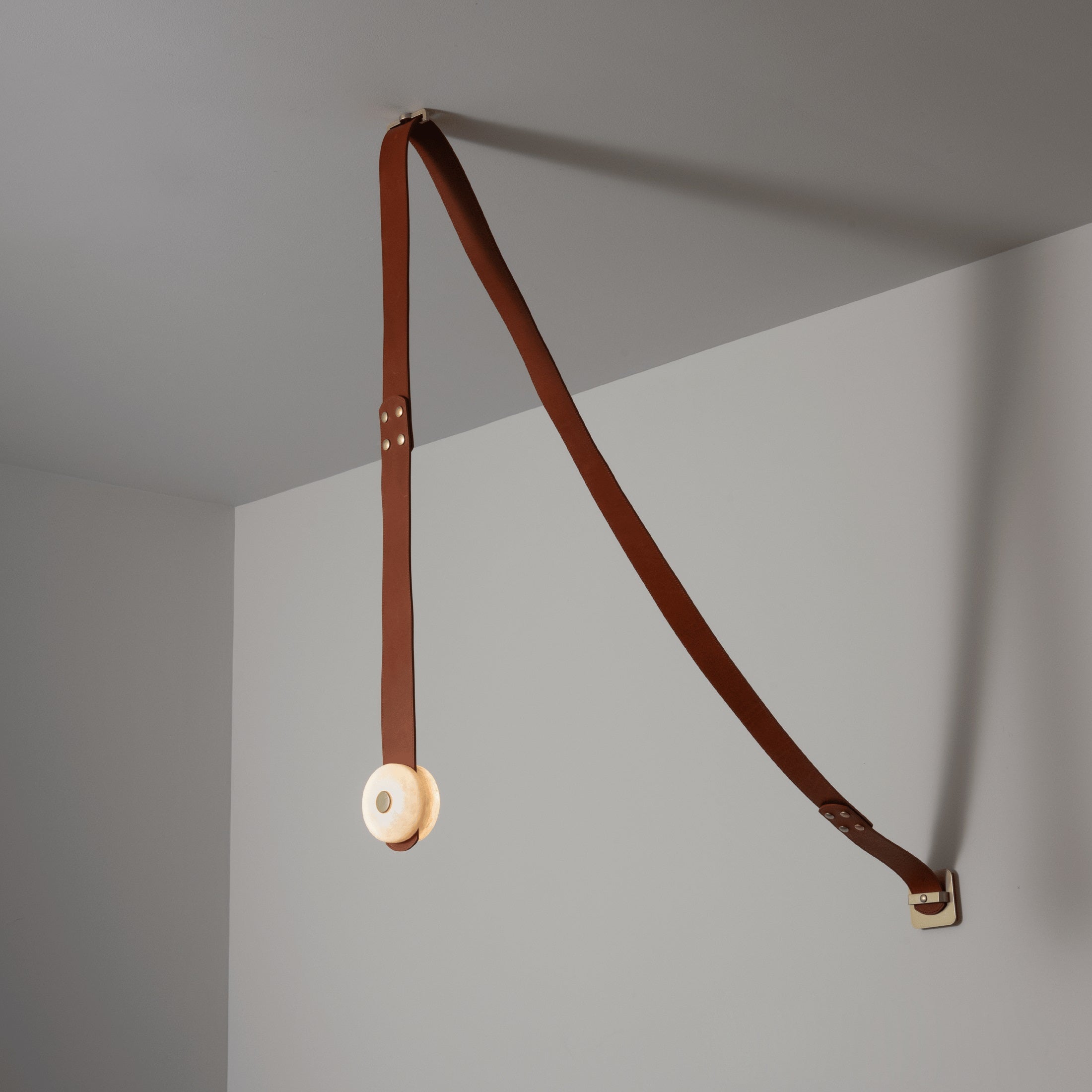 Single-head Clérachic Orinos crossing a corner, its leather strap anchored on a brass bracket fixed to the wall.