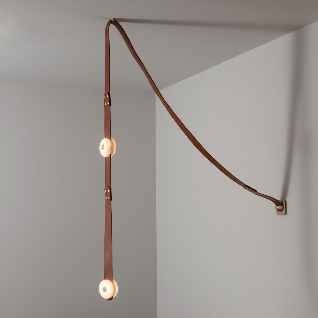 Clérachic Orinos ceiling-to-wall run with two glowing heads, leather sweeping from the wall fixing into the corner.
