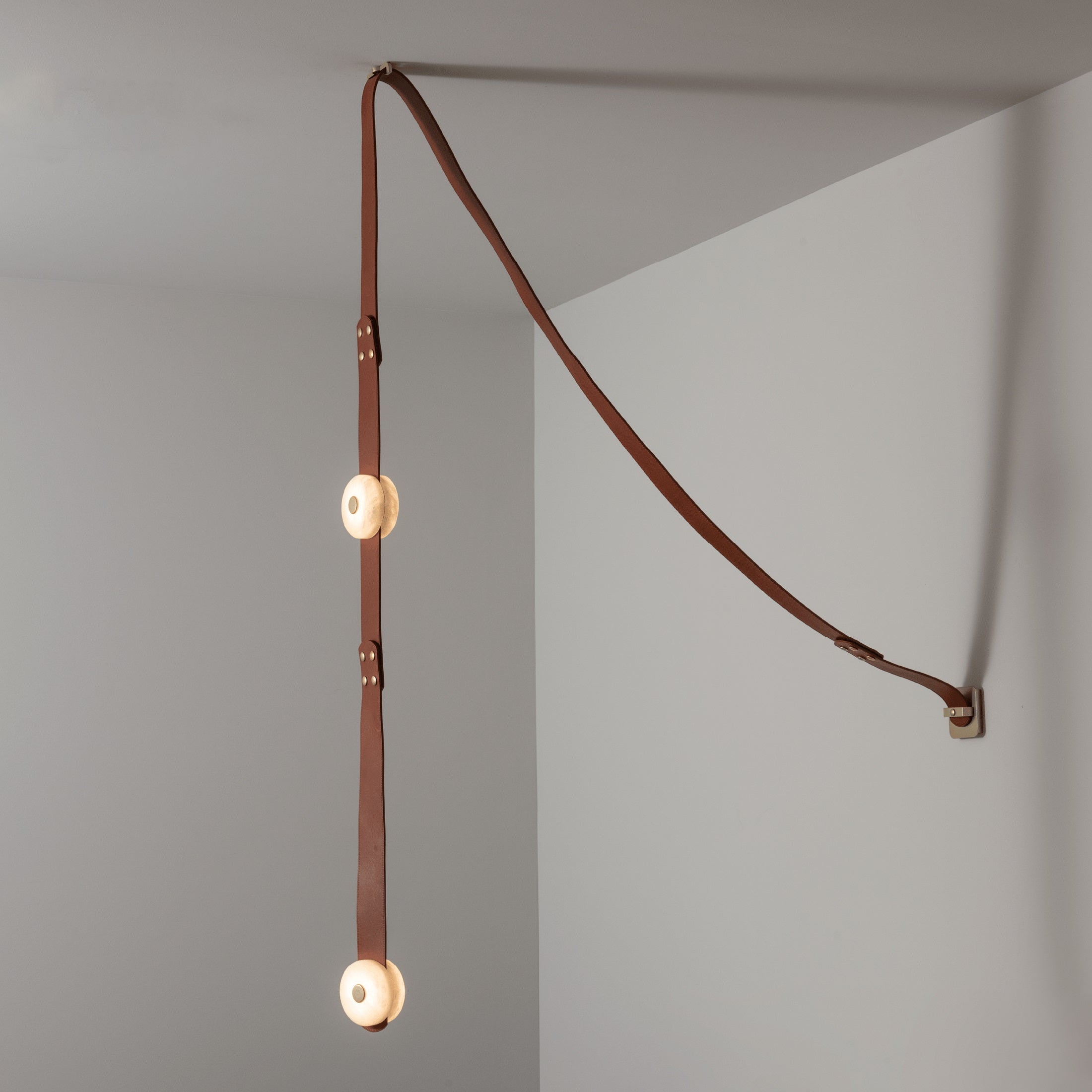 Clérachic Orinos ceiling-to-wall run with two glowing heads, leather sweeping from the wall fixing into the corner.