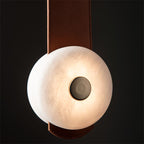 Close detail of the Clérachic Orinos disc against black — warm light through natural alabaster around a dark metal boss.