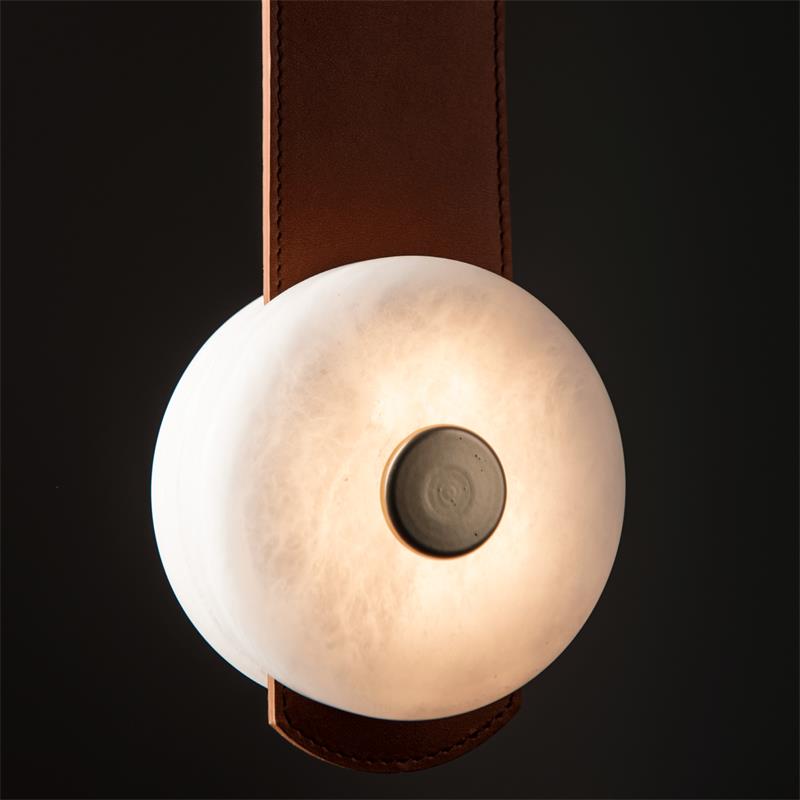 Close detail of the Clérachic Orinos disc against black — warm light through natural alabaster around a dark metal boss.