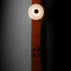 Clérachic Orinos head lit close to a grey wall, the cognac strap studded with black rivets running past the alabaster.