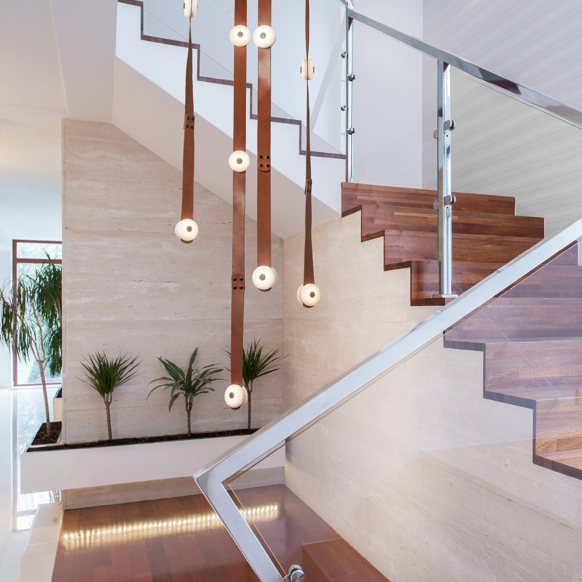 Clérachic Orinos long drops hanging through a travertine stairwell, alabaster heads lit down a double-height void.