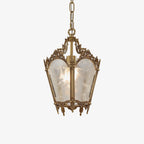 Ornate brass lantern pendant with frosted white glass panes, hung on a fine chain against a plain white backdrop, from Clérachic.