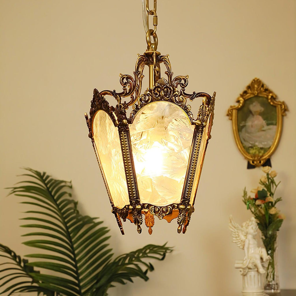 Lit brass lantern with scrolled framework and frosted glass panes, beside a palm frond and a gilt oval frame, from Clérachic.