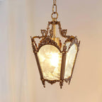 Brass lantern pendant glowing warm against a soft pink curtain, its frosted panes and chain clearly shown, from Clérachic.