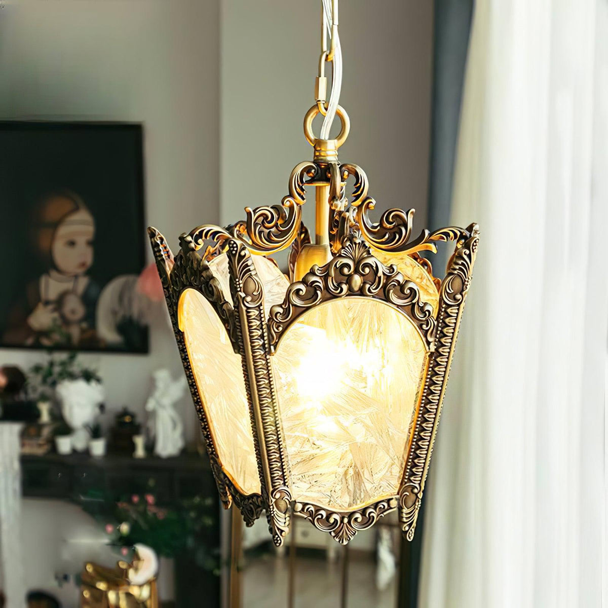 Lit Clérachic lantern pendant with a darker aged-brass frame, hung near a window with sheer curtains and a framed portrait.