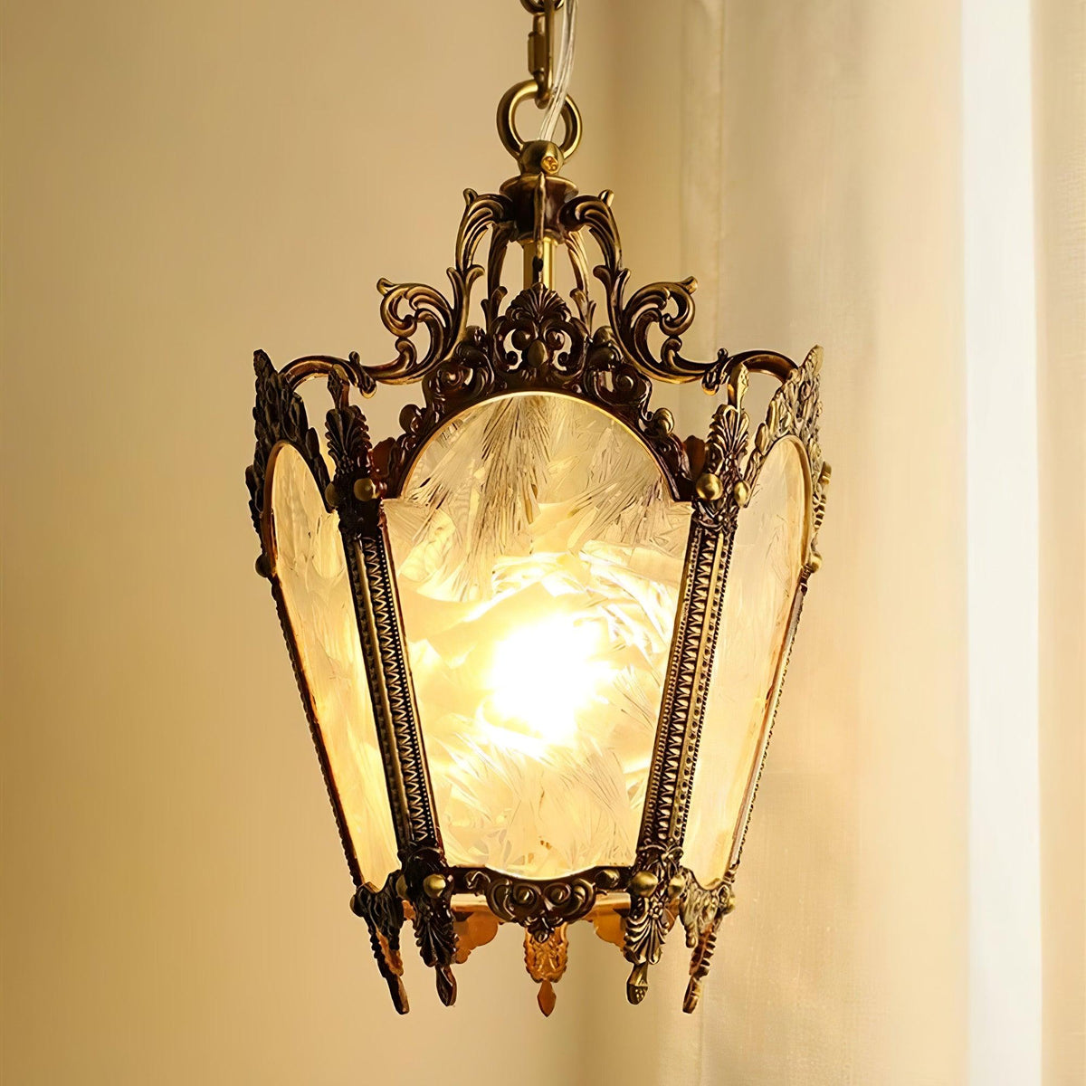 Close view of the frosted feather-pattern glass and aged brass scrollwork of this lit Clérachic lantern pendant.