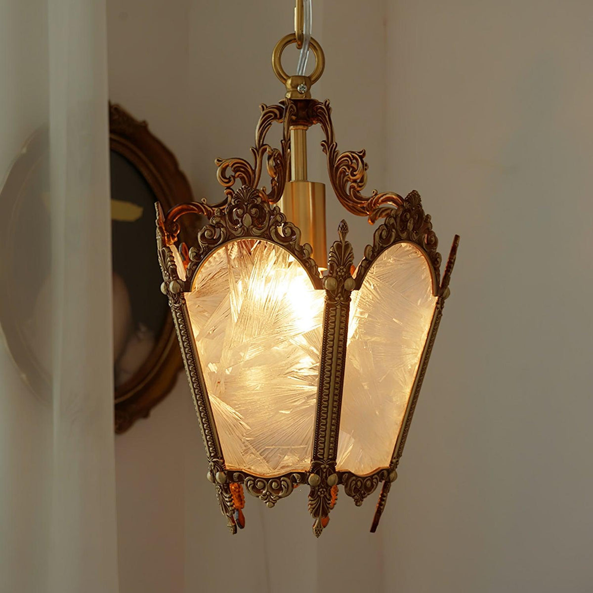 Lit brass lantern seen from slightly below, with frosted panes and scrolled corners, beside an oval frame, from Clérachic.