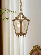 Small brass lantern pendant hung beside a sheer curtain, with a trailing green stem and a gilt frame nearby, from Clérachic.