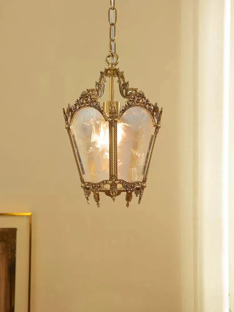 Unlit brass lantern pendant with frosted glass panes hung against a cream wall beside a framed picture, from Clérachic.