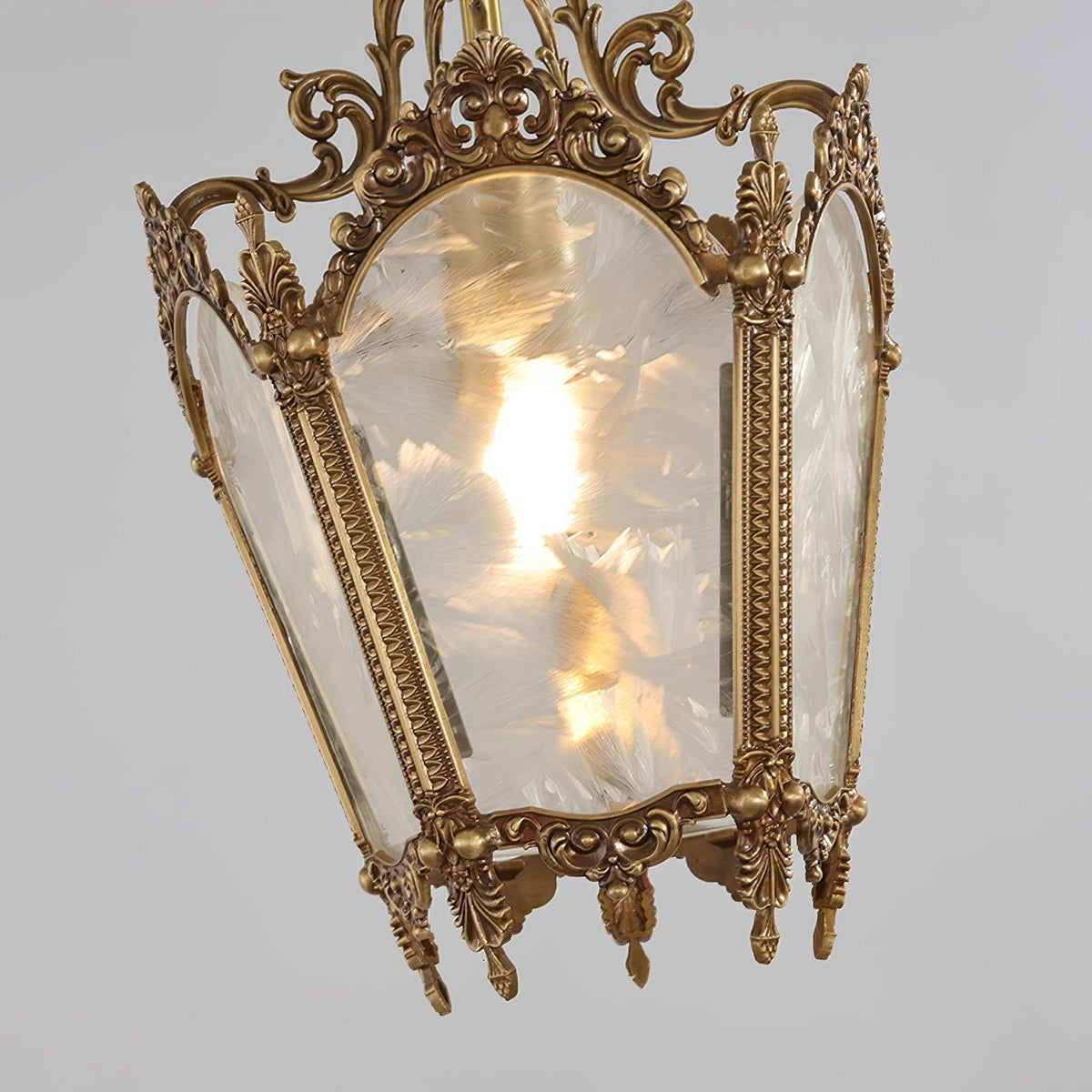 Close view of one frosted glass pane in its brass frame with scrolled crown detail, on this lit Clérachic lantern.