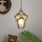 Lit brass lantern pendant above a palm frond and a small gilt frame, with an oval portrait at the corner, from Clérachic.