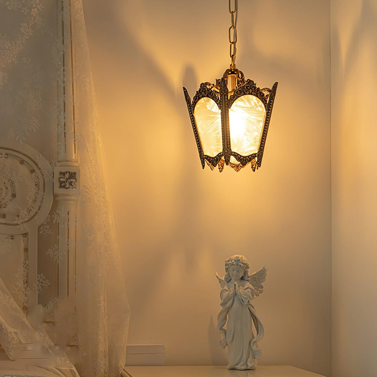 Lit brass lantern pendant casting a warm glow over a curtain and a small angel figure on a shelf, from Clérachic.