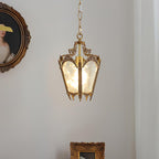 Brass lantern pendant with frosted panes hung on a pale wall near an oval portrait and a gilt frame, from Clérachic.