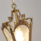 View into the top of the lit lantern, showing the brass hanging ring, the scrolled arms and the frosted glass of this Clérachic pendant.