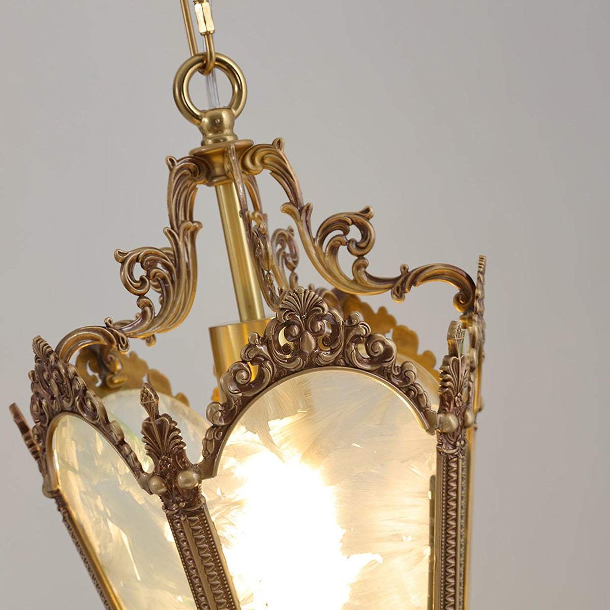 View into the top of the lit lantern, showing the brass hanging ring, the scrolled arms and the frosted glass of this Clérachic pendant.